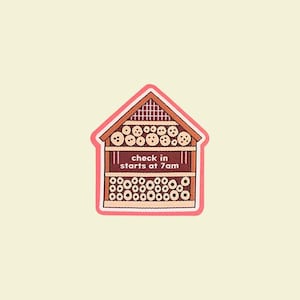 May include: A house-shaped sticker with a pink border. The house is brown and features circular openings and the text "check in starts at 7am". The background is light yellow.