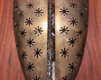 May include: A vintage brass wall sconce with a starburst pattern. The sconce has a decorative design with cut-out star shapes and a central strand of clear, faceted beads. The sconce is mounted on a wooden surface.