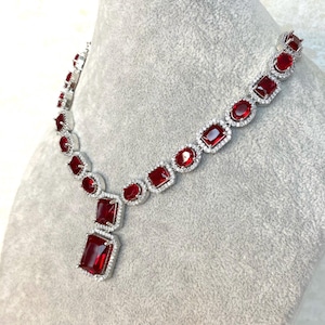 Könnte beinhalten: Eine silberne Halskette mit einem großen roten Edelstein-Anhänger. Die Halskette ist aus Silber und hat eine Kette mit kleinen roten Edelsteinen.