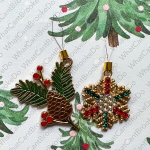 May include: Two gold-tone Christmas ornaments with a loop for hanging. One ornament is a green pine branch with red berries and a brown pine cone. The other ornament is a gold snowflake with red and green accents and clear rhinestones.