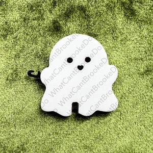 May include: White ghost-shaped ornament with black eyes and a heart-shaped mouth. The ornament has the text "What Can't Brooke Do" written on it.