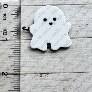 May include: A white ghost with black eyes and a smiling mouth. The ghost is about 1 inch tall and is made of a smooth, white material.