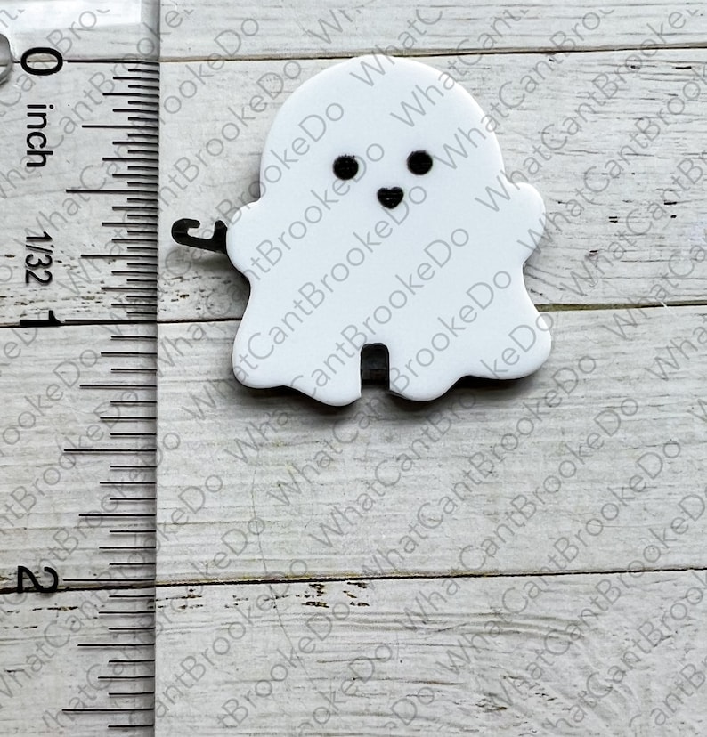 May include: A white ghost with black eyes and a smiling mouth. The ghost is about 1 inch tall and is made of a smooth, white material.