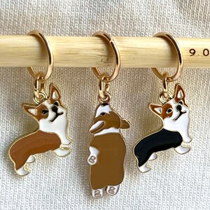 May include: Three gold stitch markers with a 9.0 mm needle size label. Each marker features a different colored enamel corgi design: brown and white, brown, and black and white.