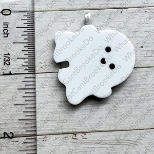 May include: White ghost-shaped ornament with black eyes and a mouth. The ornament is about 1 inch in size and is made of ceramic.