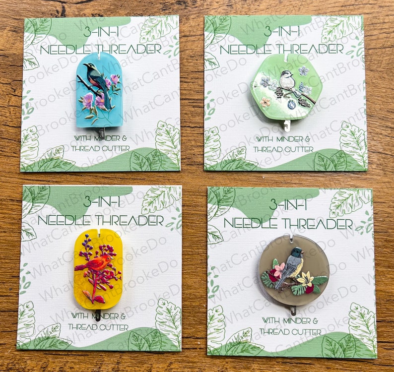 May include: Four 3-in-1 needle threaders with a bird design. Each threader has a different coloured background and bird design. The text "3-in-1 Needle Threader" and "With Minder & Thread Cutter" is printed on each card.