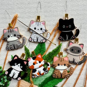 May include: Six adorable cat-shaped needle threaders with gold accents. Each cat is a different color and pattern, including gray tabby, black, calico, brown tabby, and Siamese.