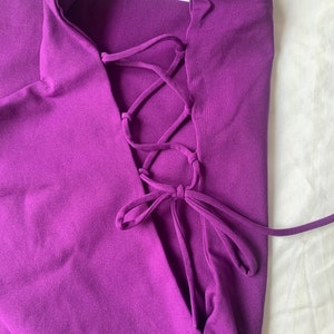 May include: Purple halter top with a lace-up back detail. The top is made of a soft, stretchy fabric.