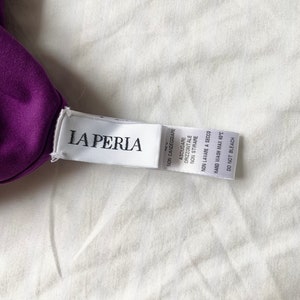 May include: A white tag with the text "LA PERIA" in black lettering. The tag has care instructions in Italian, including "NON CANDEGGIARE" (Do not bleach), "ASCIUGARE ORIZZONTALE" (Horizontal drying), "NON STIRARE" (Do not iron), "NON LAVARE A SECCO" (Do not dry clean), and "HAND WASH MAX 40&deg;C" (Hand wash at a maximum of 40 degrees Celsius).