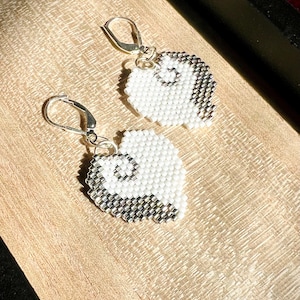 May include: A pair of heart-shaped earrings crafted from small white and metallic silver beads. Each earring features a split design with a white section and a metallic silver section, suspended from silver-toned metal leverback ear wires.