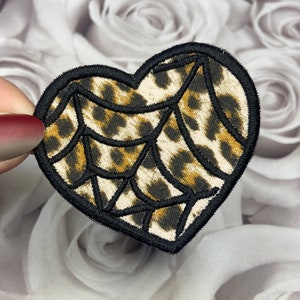 May include: A black and brown heart-shaped patch with a spiderweb design on a leopard print background.