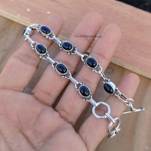 May include: A silver bracelet with black oval gemstones and a toggle clasp. The bracelet is made of sterling silver and features a delicate chain design.