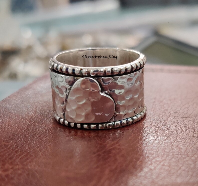 Pu&ograve; includere: Un anello d'argento con finitura martellata e un design a forma di cuore. L'anello &egrave; inciso con le parole "Silverartisan Ring".