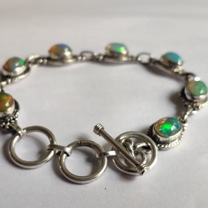 May include: A silver bracelet with a toggle clasp and oval-shaped opal stones in shades of green, blue, and orange.