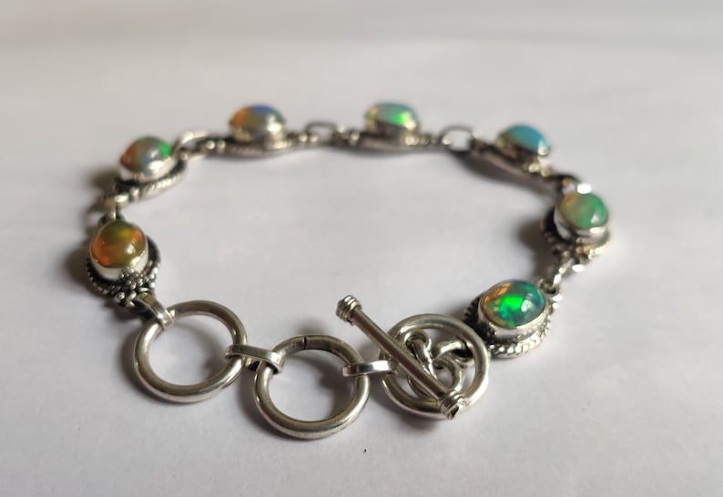 May include: A silver bracelet with a toggle clasp and oval-shaped opal stones in shades of green, blue, and orange.