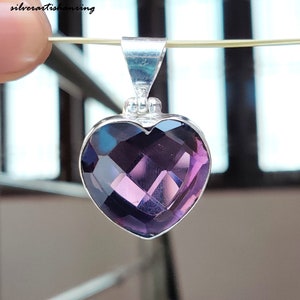 Könnte beinhalten: Ein silberner herzförmiger Anhänger mit einem violetten Edelstein. Der Edelstein ist facettiert und hat eine tiefe violette Farbe.