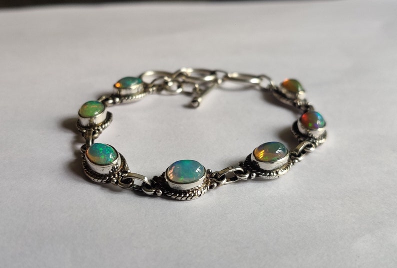 May include: A silver bracelet with a chain link design and oval-shaped opal stones. The stones have a rainbow iridescent effect.