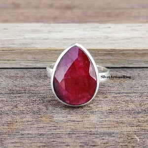 Könnte beinhalten: Ein tropfenförmiger Rubinring, der in Sterlingsilber gefasst ist. Der Rubin ist tiefrot und hat einen facettierten Schliff.