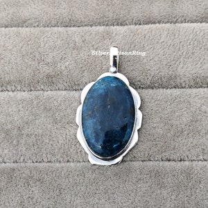 K&ouml;nnte beinhalten: Ein silberner Anh&auml;nger mit einem blauen Edelstein, der in einen silbernen ovalen Rahmen gefasst ist. Der Anh&auml;nger hat eine &Ouml;se zum Anbringen einer Kette.