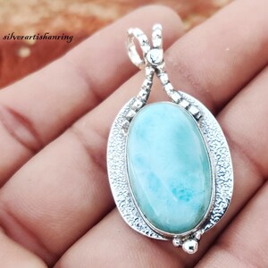 May include: A silver pendant with a light blue oval-shaped gemstone. The pendant has a detailed silver design around the gemstone.