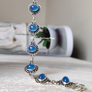 May include: A silver bracelet with five blue oval-shaped stones set in silver bezels. The bracelet has a lobster clasp closure.