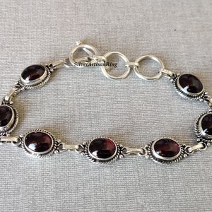 May include: A silver bracelet with a chain link design and six oval-shaped red gemstones. The bracelet has a lobster claw clasp.