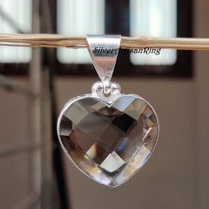 May include: A silver heart-shaped pendant with a clear smoky quartz gemstone. The pendant is hanging from a branch.