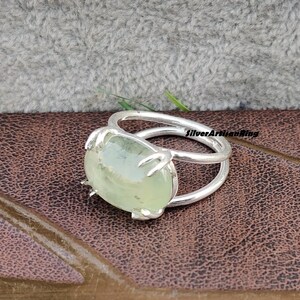 May include: A silver ring with a green gemstone set in a claw setting. The ring has a double band design.