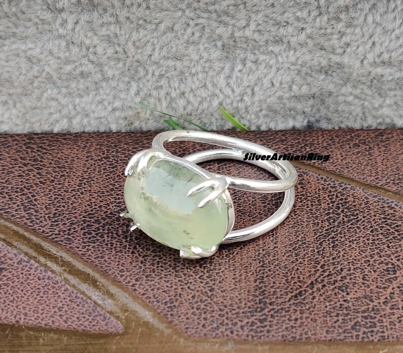 May include: A silver ring with a green gemstone set in a claw setting. The ring has a double band design.