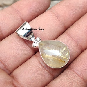 May include: A teardrop-shaped pendant with a silver bail. The pendant features a clear, faceted gemstone with golden inclusions. The gemstone is set in a silver bezel. The text "Silver Artisan Ring" is visible on the image.