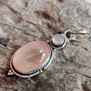May include: A silver pendant featuring a large oval-shaped rose quartz gemstone with a smaller round rose quartz gemstone above it. The pendant has a silver bail for attaching to a chain.