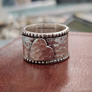 Pu&ograve; includere: Un anello d'argento con finitura martellata e un design a forma di cuore. L'anello &egrave; inciso con le parole "Silverartisan Ring".