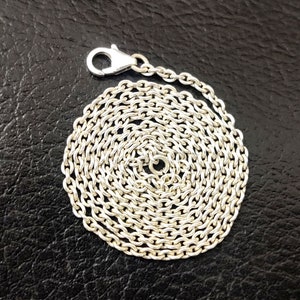Puede incluir: Un collar de cadena de plata con cierre de langosta. La cadena est&aacute; enrollada en un c&iacute;rculo.