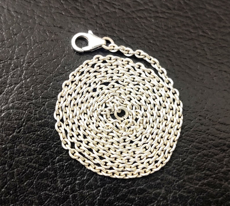 Puede incluir: Un collar de cadena de plata con cierre de langosta. La cadena est&aacute; enrollada en un c&iacute;rculo.