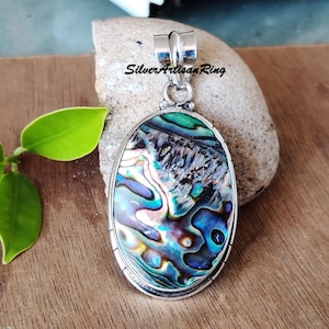 May include: A silver pendant featuring a large oval abalone shell with iridescent blue, green, and purple colors. The pendant has a silver bail for attaching to a chain.