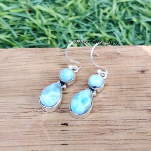 May include: A pair of silver dangle earrings with two teardrop-shaped blue labradorite stones on each earring.