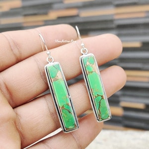 May include: A pair of silver dangle earrings featuring green turquoise stones. The stones are rectangular and have a marbled pattern.