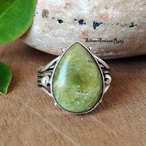 Peut inclure: Une bague en argent avec une pierre précieuse verte sertie en forme de goutte. La bague a une bande torsadée avec de petites perles d'argent.