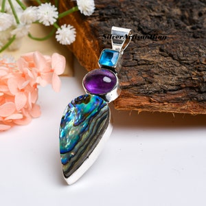 May include: A silver pendant with a teardrop-shaped abalone shell, a round amethyst gemstone, and a square blue topaz gemstone.