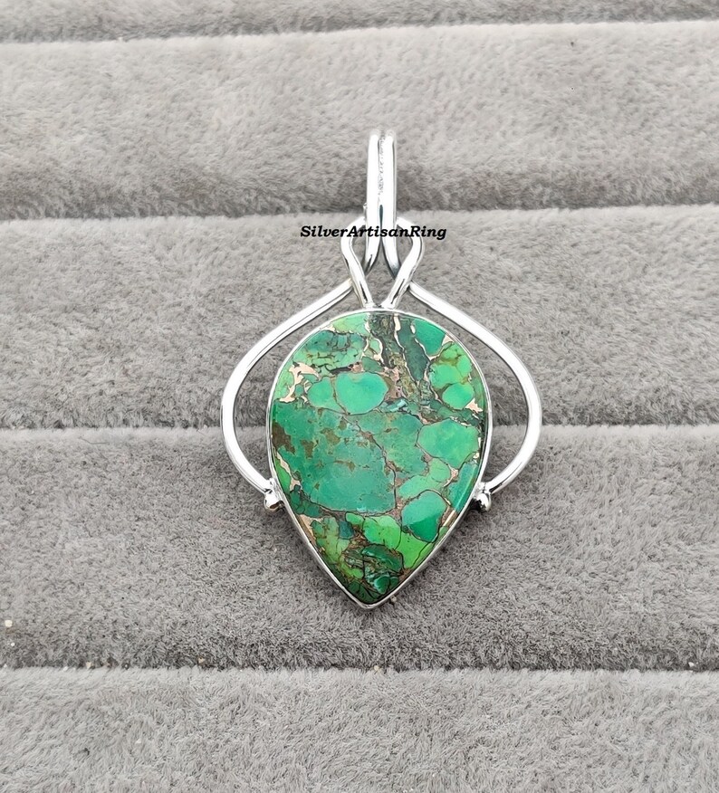 May include: A silver pendant featuring a green and brown gemstone in a teardrop shape. The pendant is set in a silver bail with a loop for attaching a chain.