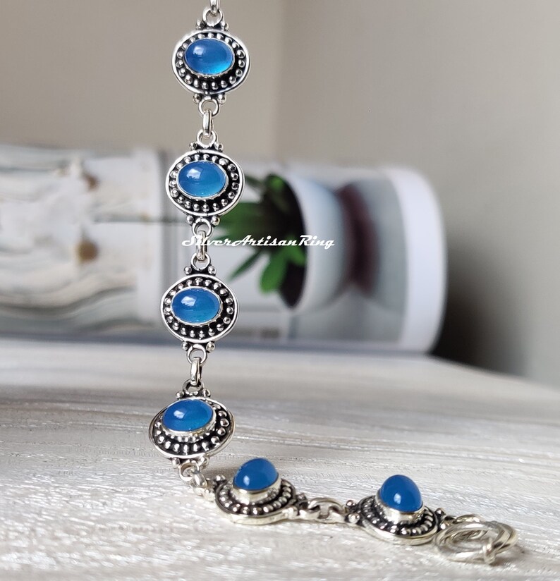 May include: A silver bracelet with five blue oval-shaped stones set in silver bezels. The bracelet has a lobster clasp closure.