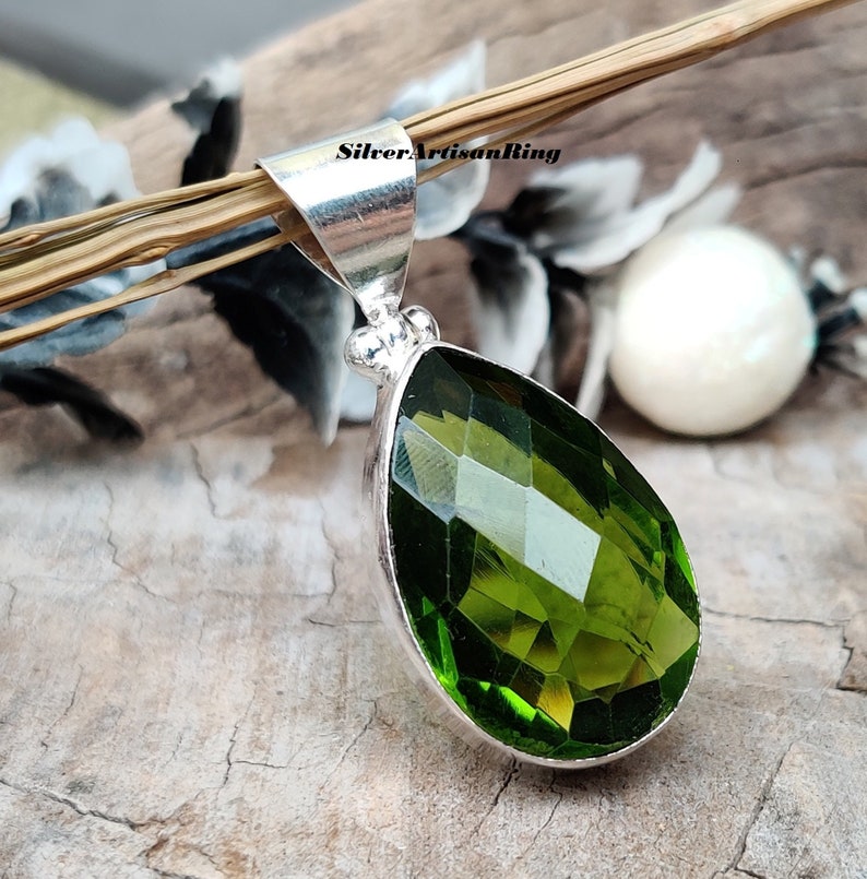 May include: A teardrop-shaped green gemstone pendant with a silver bail. The gemstone is faceted and has a high polish.