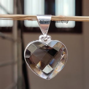 May include: A silver heart-shaped pendant with a clear smoky quartz gemstone. The pendant is hanging from a branch.