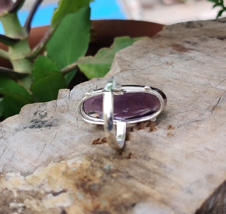 May include: A silver ring with a large oval amethyst gemstone. The ring is set in a simple band and the stone is faceted.