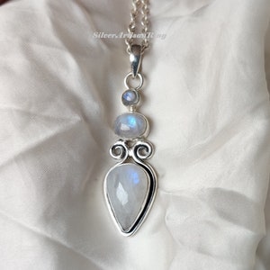 May include: A silver necklace with a pendant featuring three moonstone gems. The pendant has a teardrop shape with a swirl design.