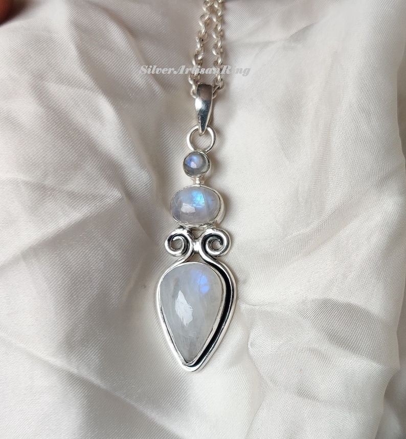 May include: A silver necklace with a pendant featuring three moonstone gems. The pendant has a teardrop shape with a swirl design.
