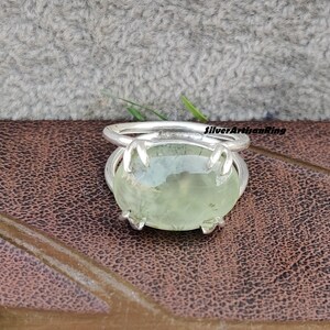 May include: A silver ring with a green gemstone. The ring has a claw setting and the gemstone is oval shaped.