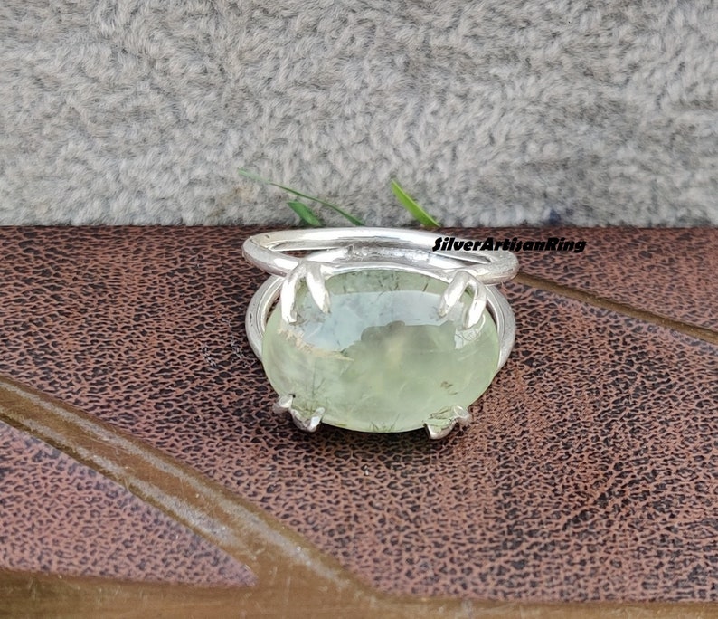 May include: A silver ring with a green gemstone. The ring has a claw setting and the gemstone is oval shaped.