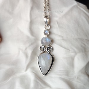 May include: A silver necklace with a teardrop-shaped moonstone pendant. The pendant is surrounded by two smaller moonstones and intricate silver detailing.