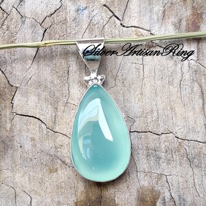 May include: A teardrop-shaped pendant featuring a light blue chalcedony gemstone set in sterling silver.